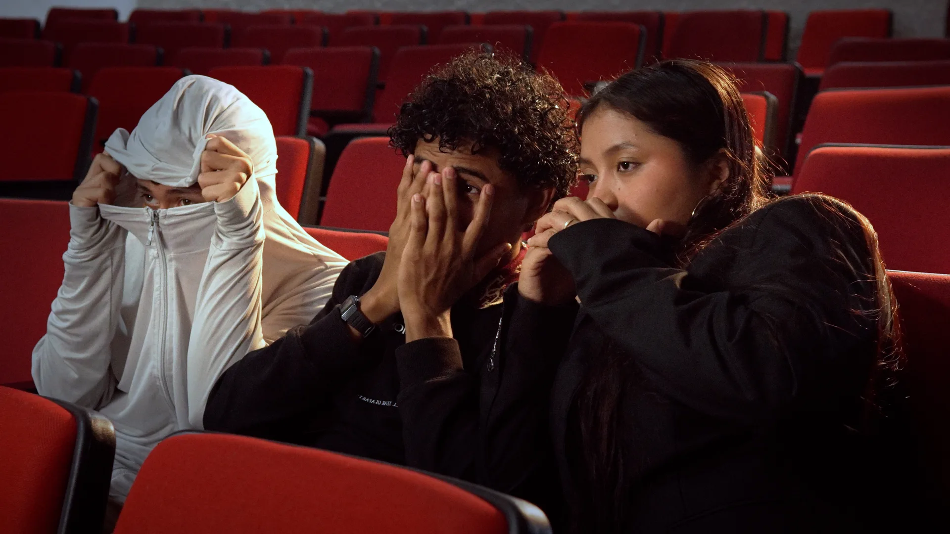 Tres jóvenes reaccionan asustados mientras miran hacia la pantalla del cine.
